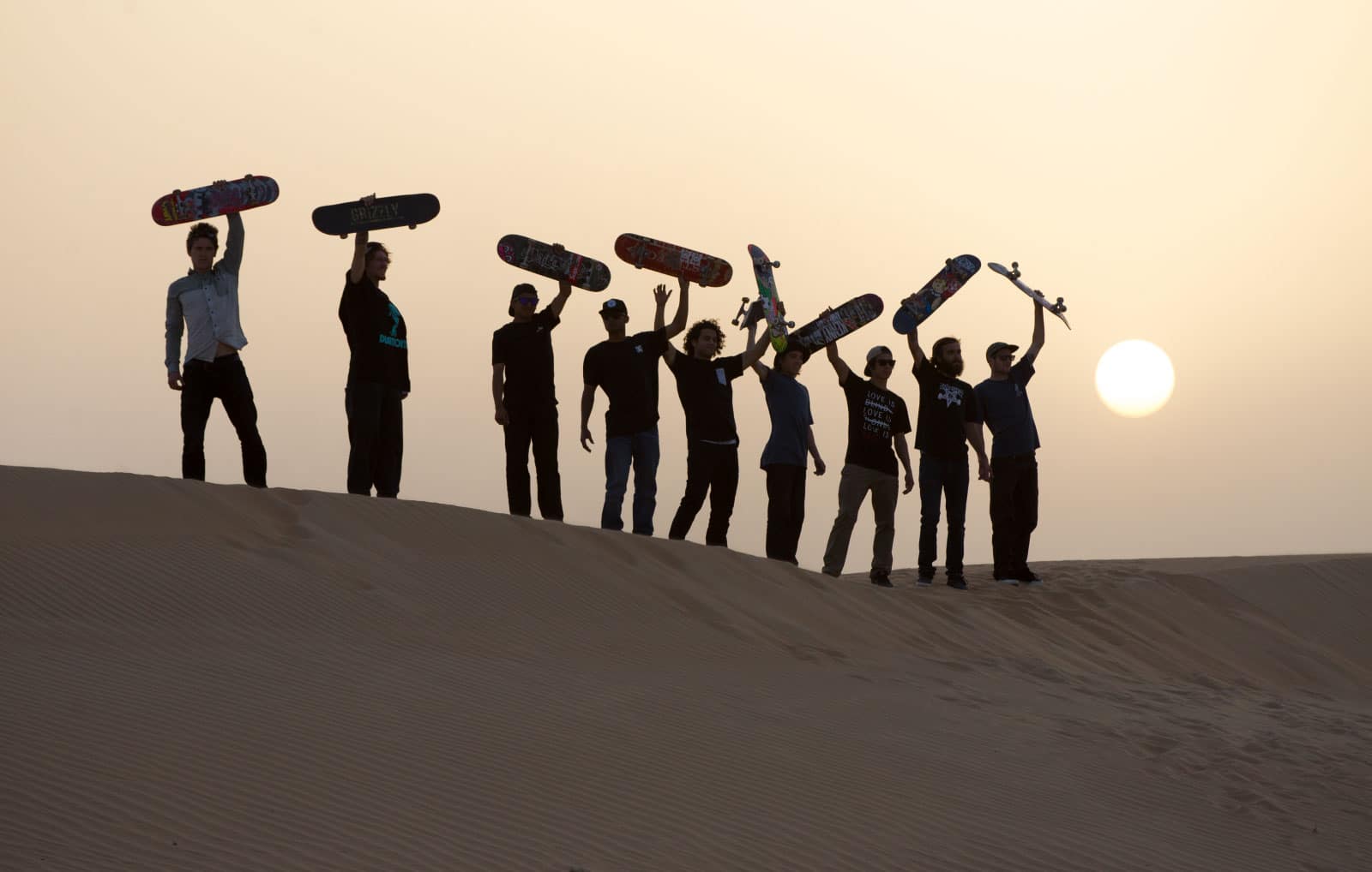 skateboarders on a sand dune holding boards in the air
