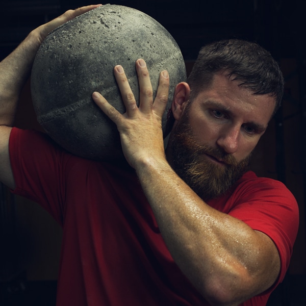 Athlete lifting large concrete ball on shoulder